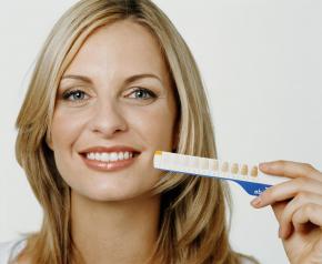 A woman holding up a whitening gauge to show how in office teeth whitening can brighten your smile