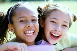 Two young girls hugiing playfully with growing smiles to show that vitamin d can help with cavities